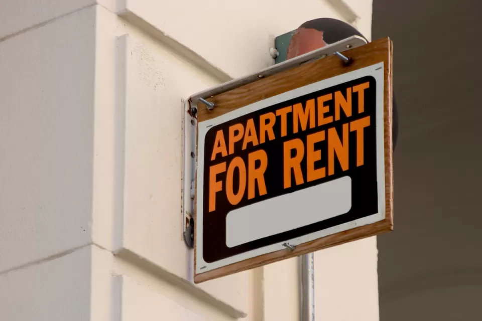 Close-up of black, white, and orange APARTMENT FOR RENT sign on building.